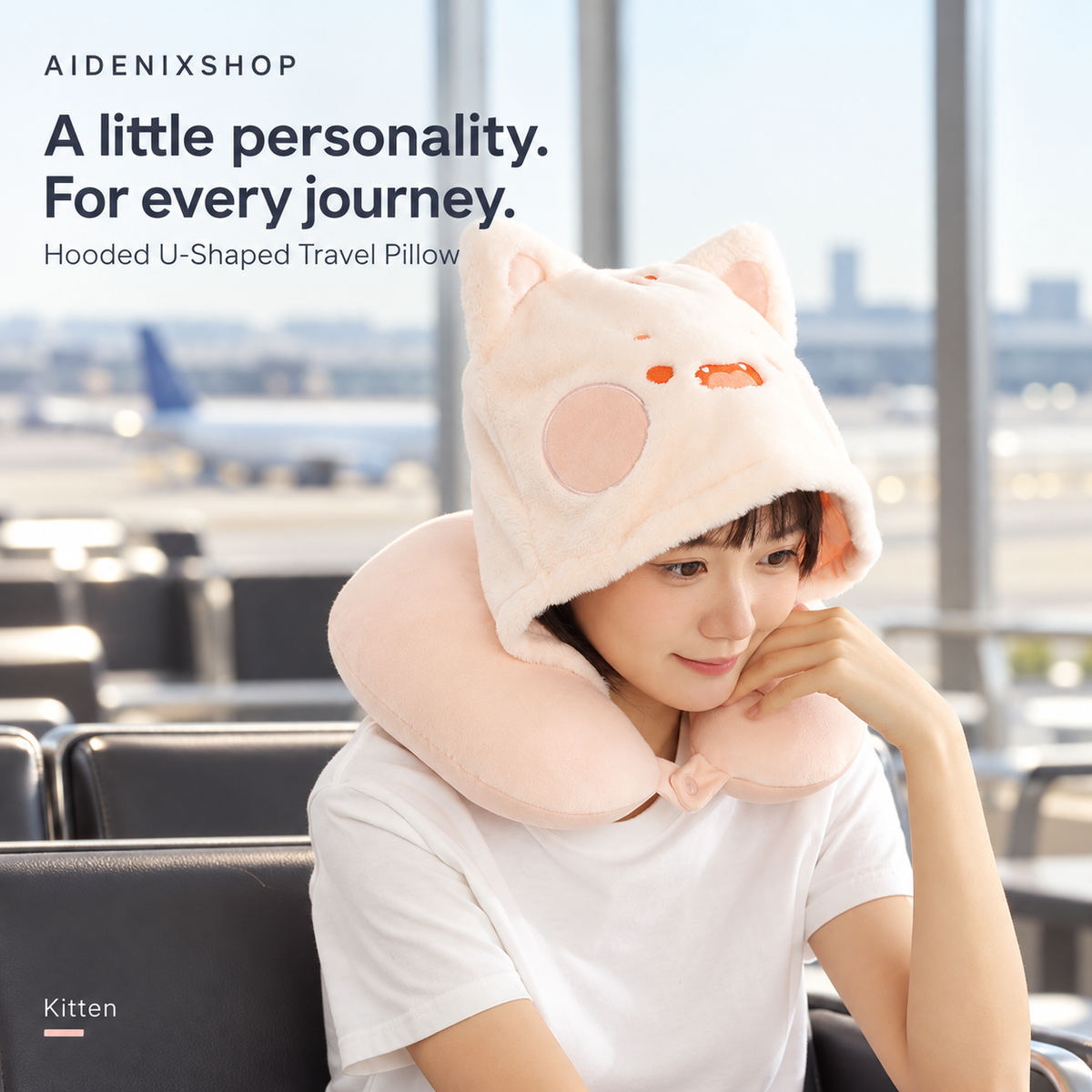 Person wearing the pink Kitten hooded U-shaped travel pillow against an airport backdrop in an Aidenixshop advertisement